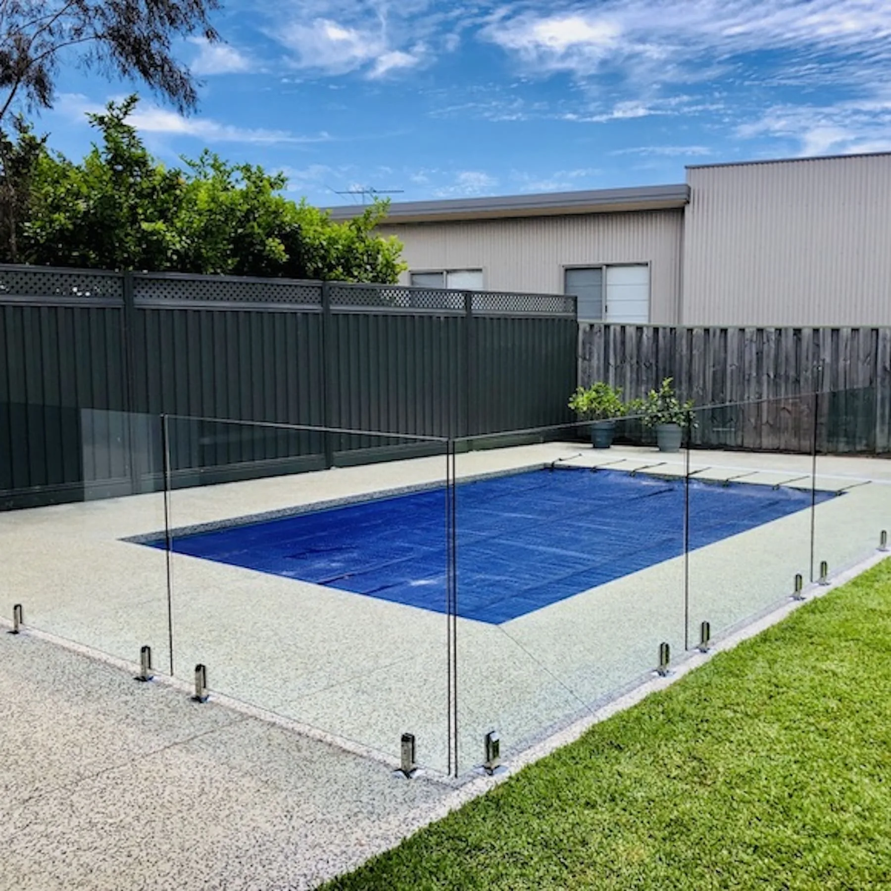 Frameless glass pool fence around a covered pool on a lawn