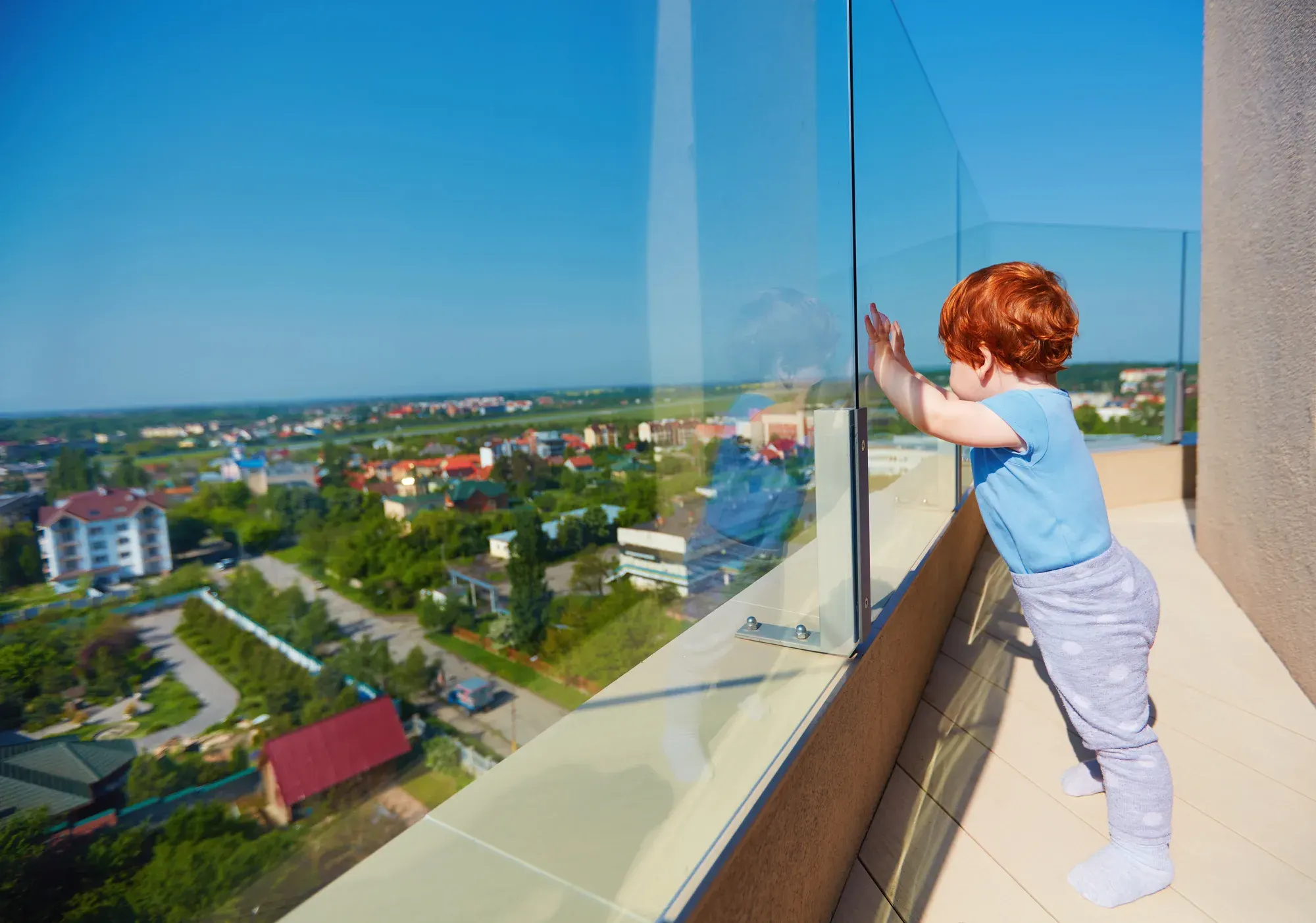 Toddler looking through a glass balustrade on a high-rise balcony
