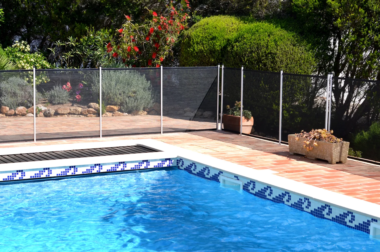 Glass pool fence panels around a tiled pool with garden beds