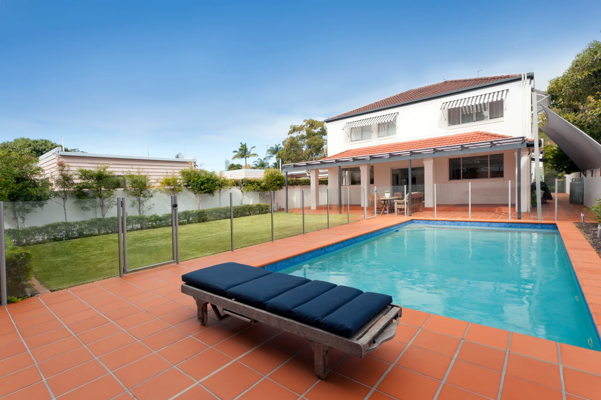 Glass pool fence around a backyard pool with a sun lounge