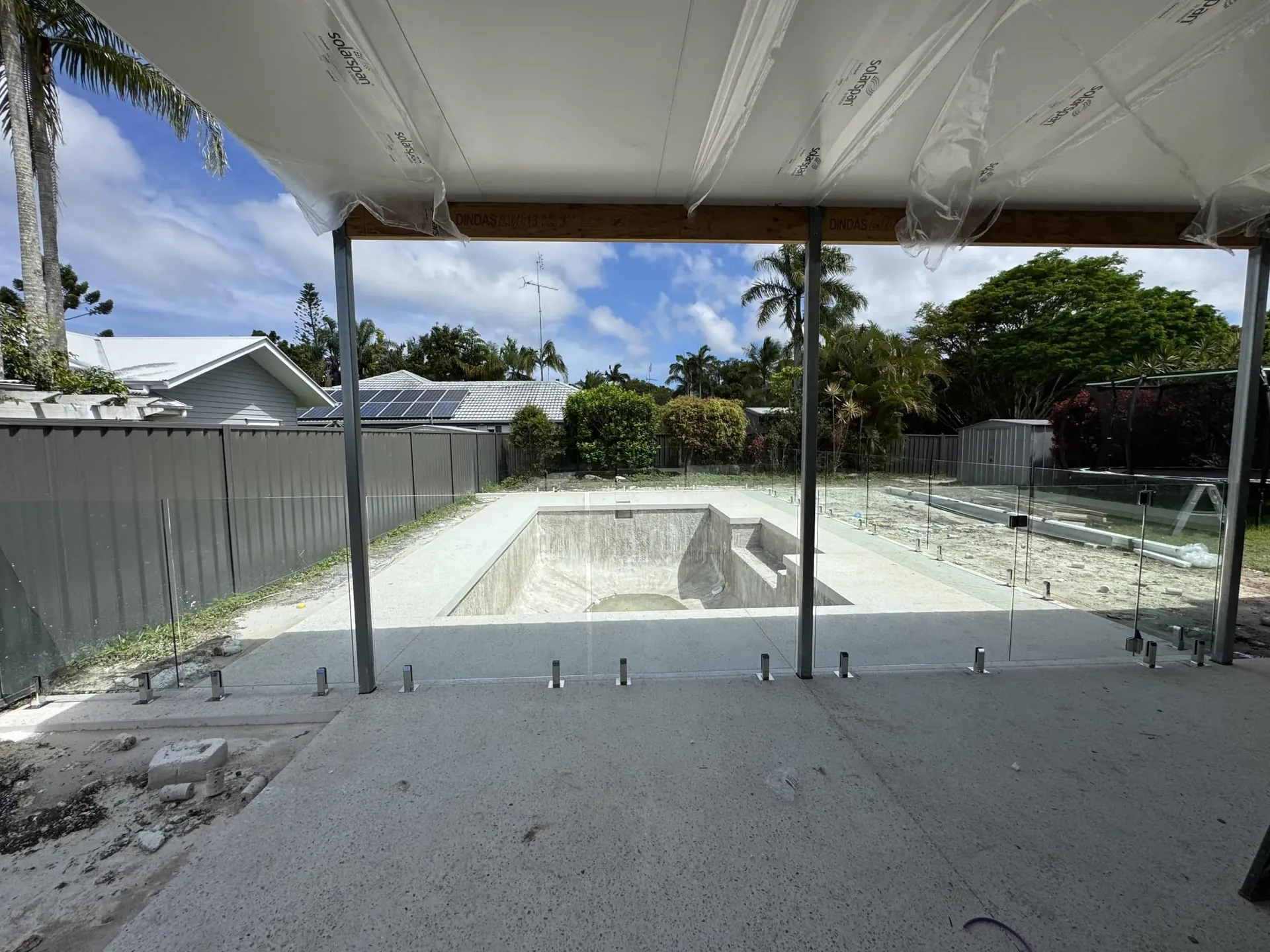 Completed glass pool fence around a new pool beside a covered patio