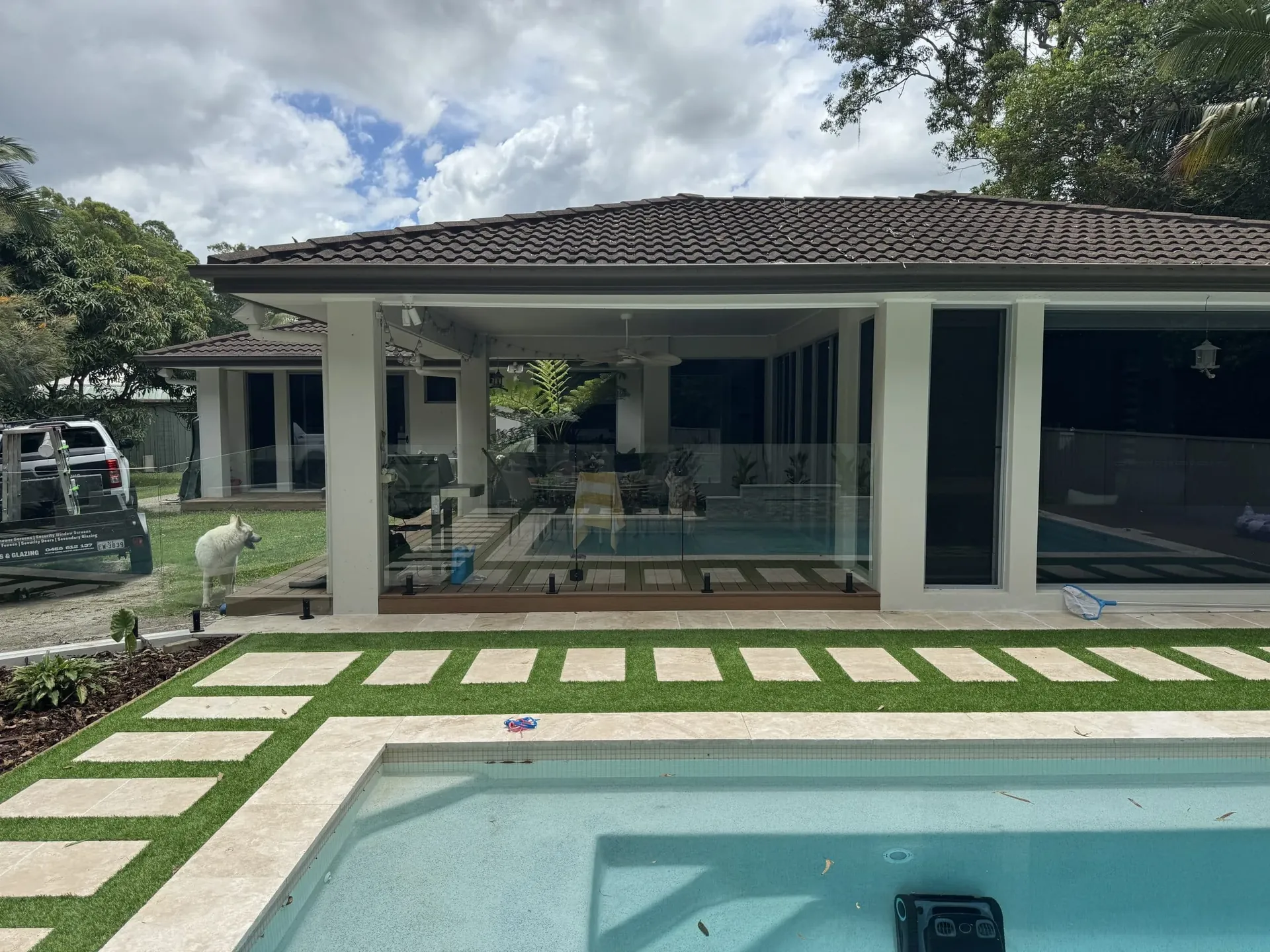 Frameless glass pool fence across a pool with a stepping-stone lawn