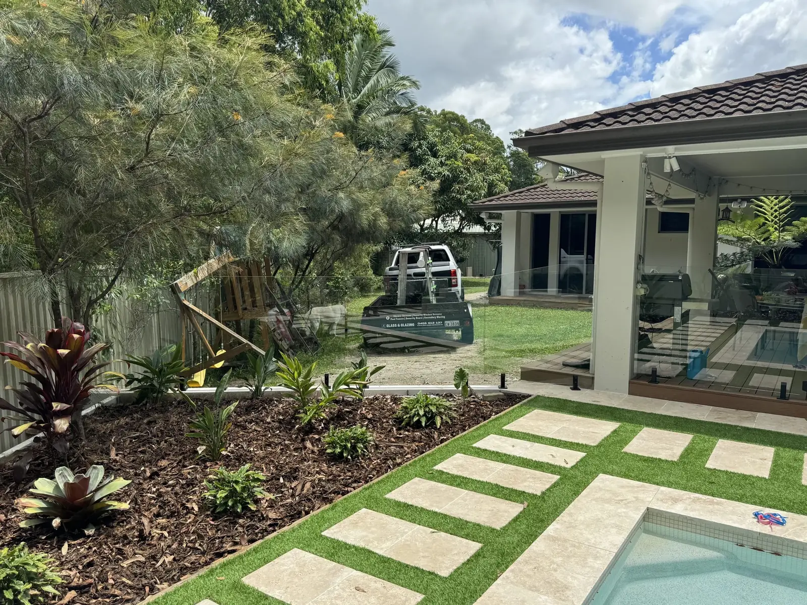 Frameless glass pool fence beside a landscaped garden and stepping stones