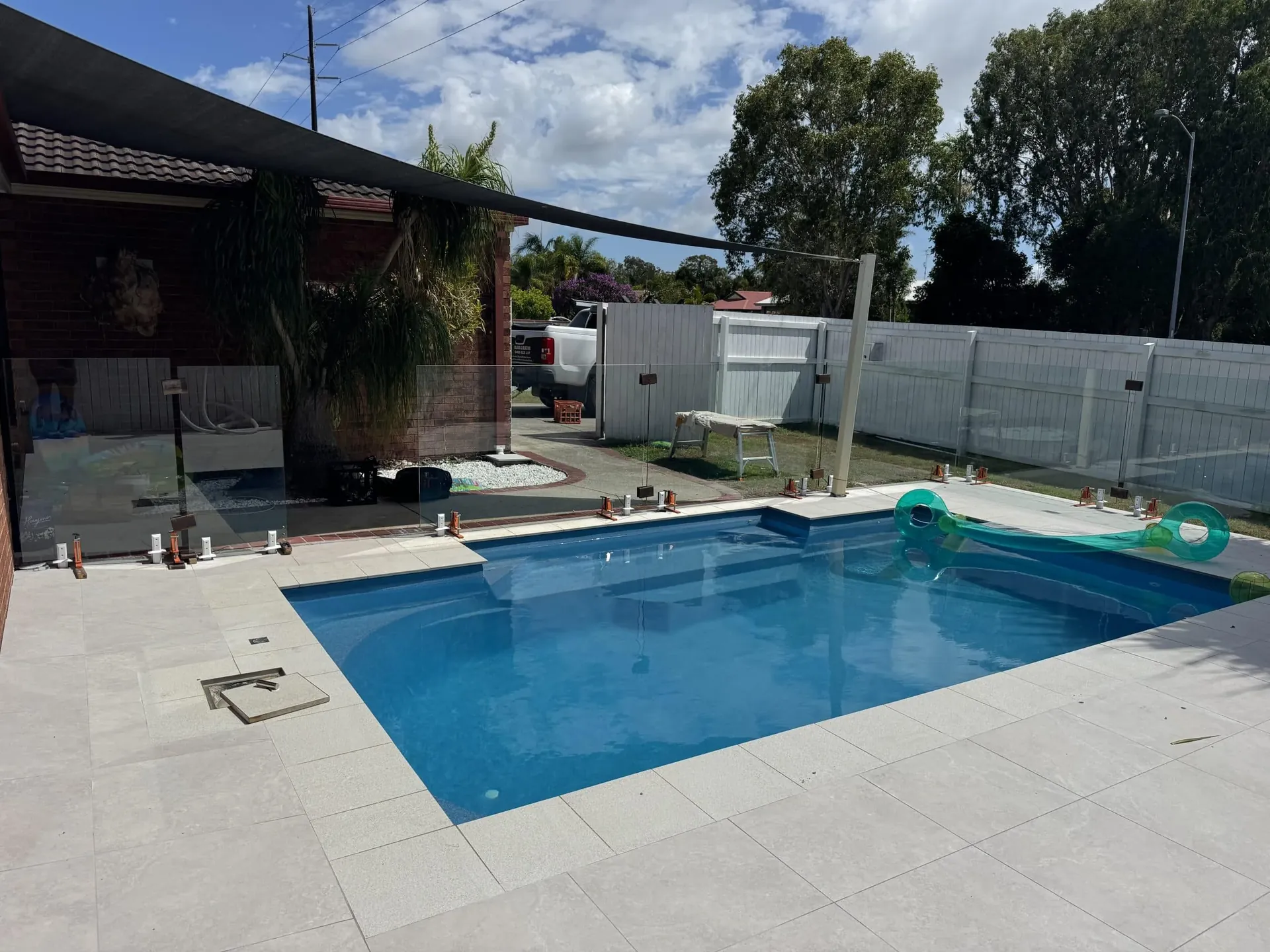 Frameless glass pool fence around a blue-tiled pool