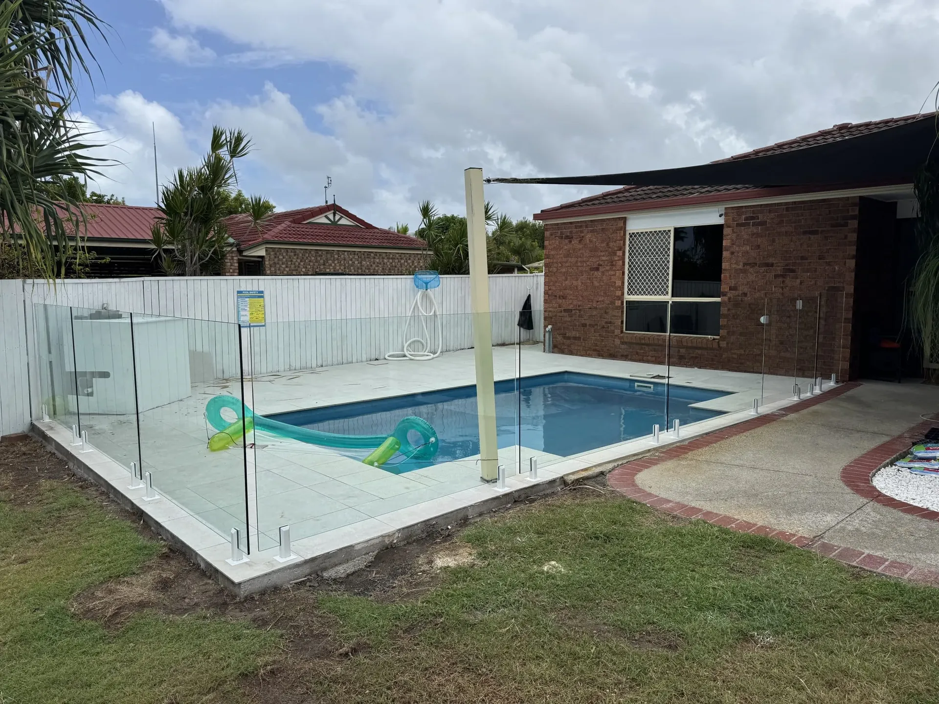 Frameless glass pool fence around a backyard pool at a brick home