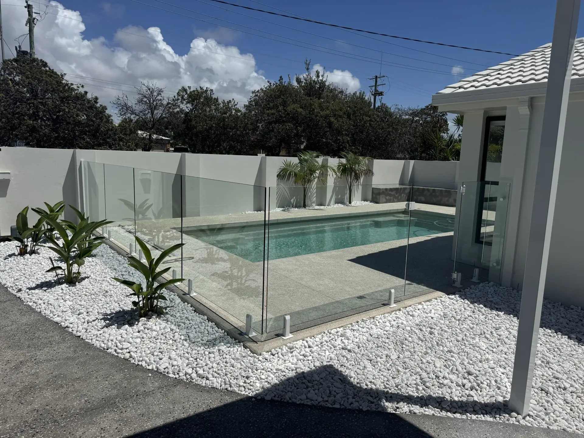 Frameless glass pool fencing beside a pool cabana and garden