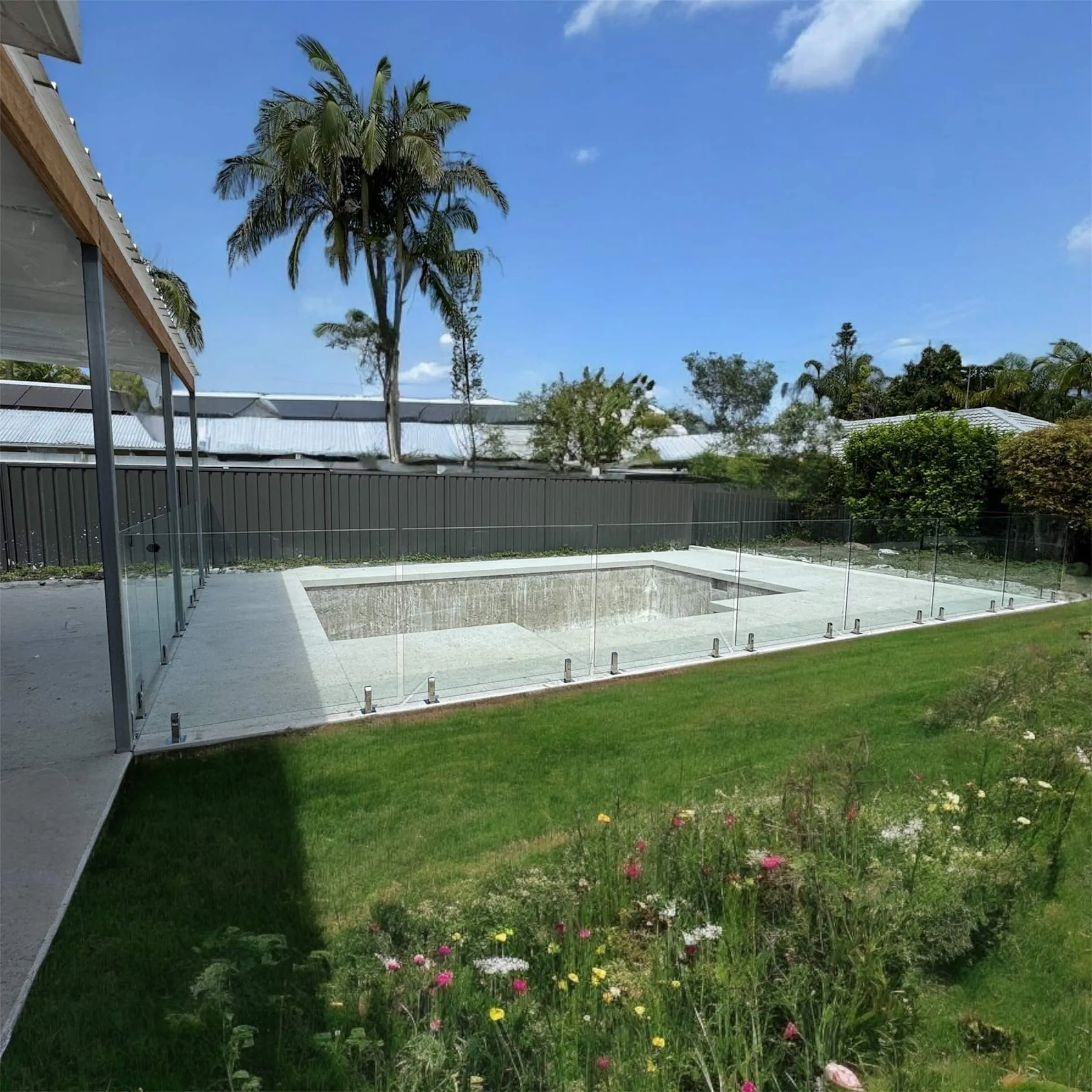 Glass pool fence around a pool beside a wildflower lawn