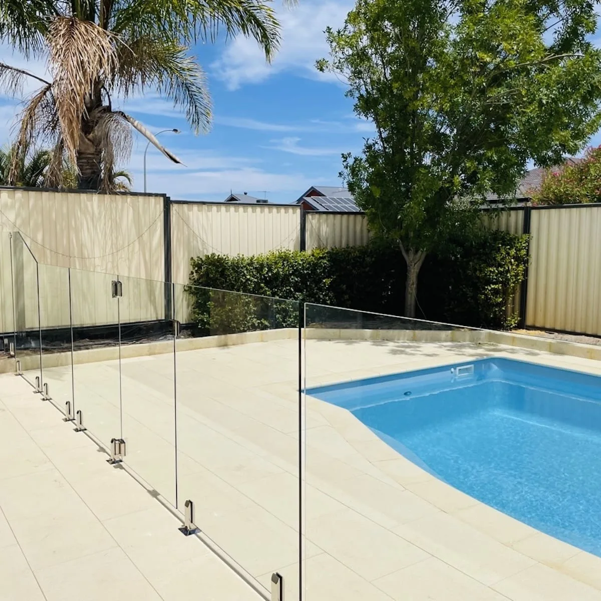 Frameless glass pool fence around a pool with a garden backdrop
