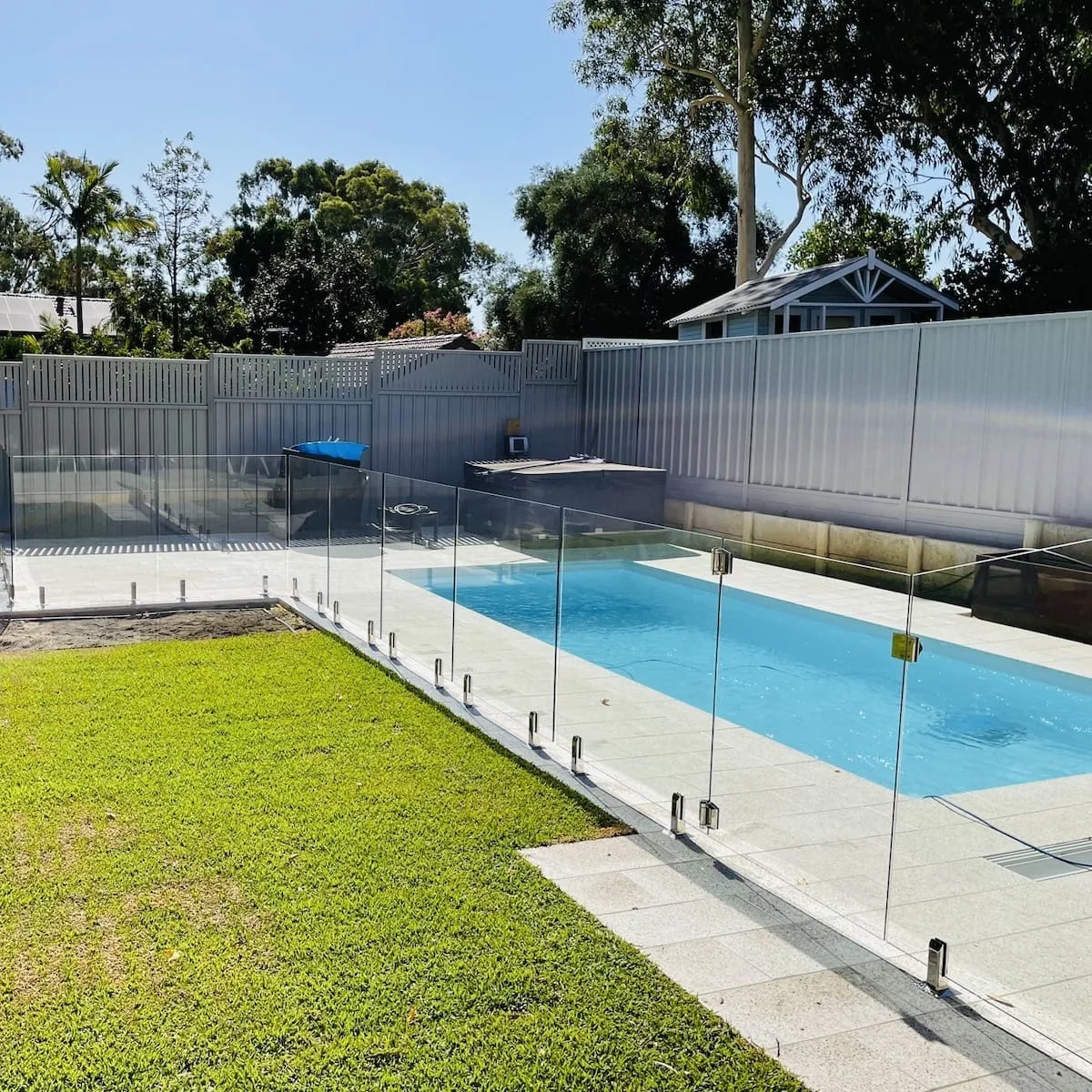 Frameless glass pool fence beside a lawn and narrow pool