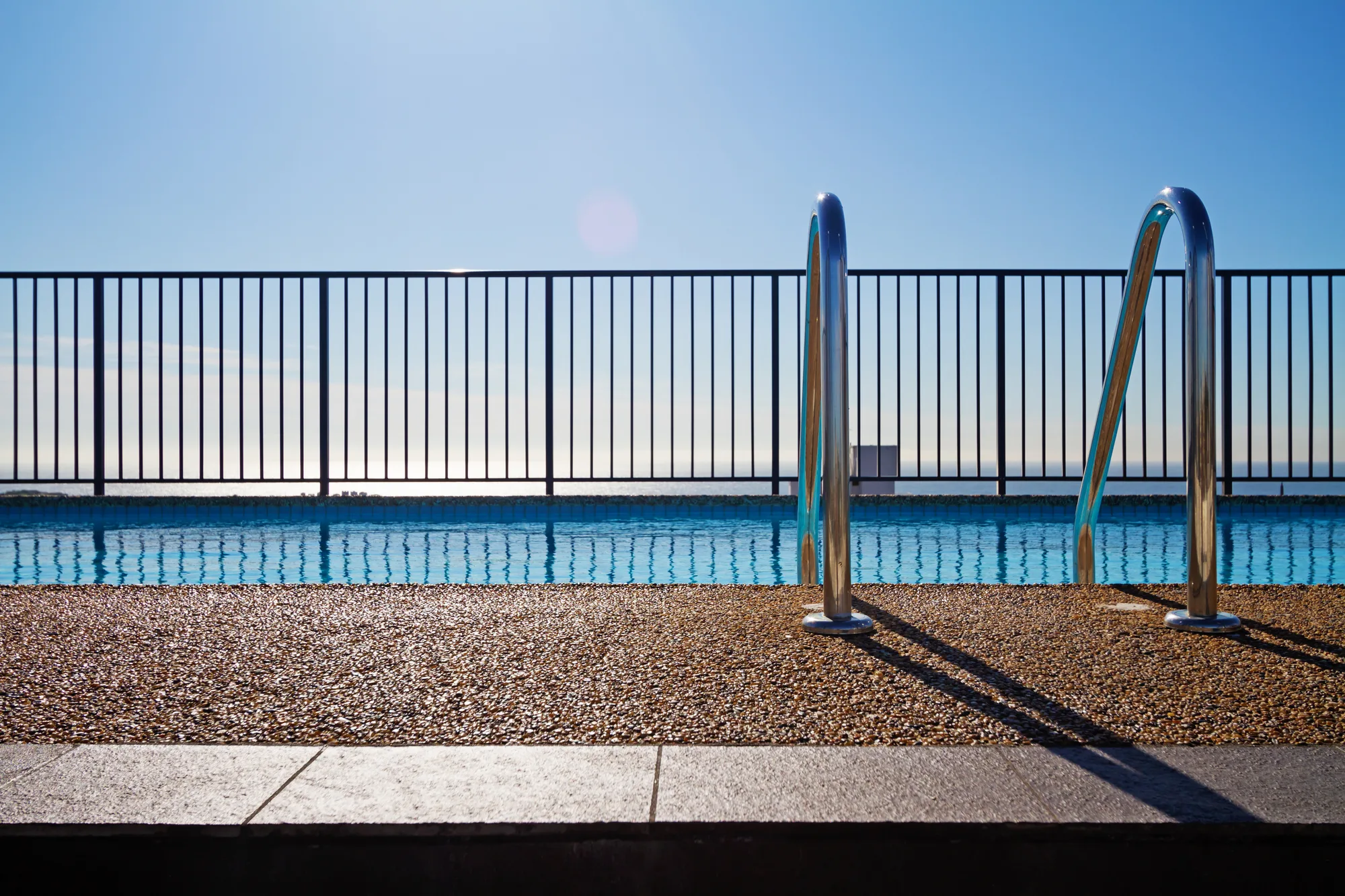 Black tubular pool fencing beside a pool ladder